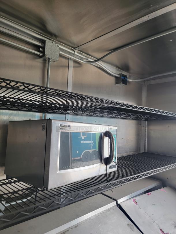 Sharp commercial microwave on metal shelf, Model R-22GV, stainless steel, in good condition with visible power cord and controls.