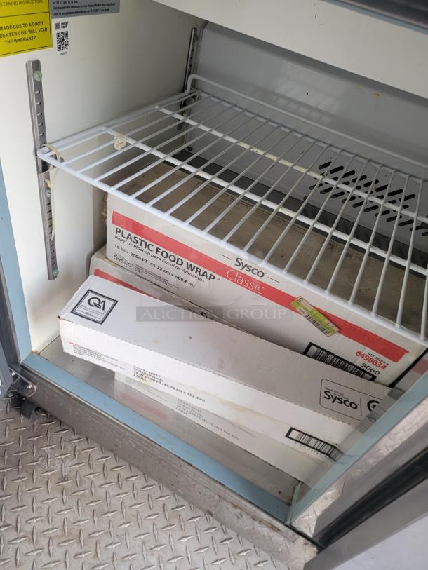 Sysco plastic food wrap rolls on metal shelf. Boxes labeled "Sysco Classic" and dimensions listed. Shelf in fair condition.