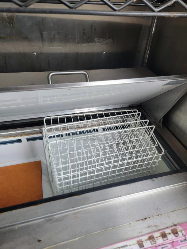 Commercial-grade metal basket in a stainless steel industrial freezer, clean condition. Basket has a grid pattern.