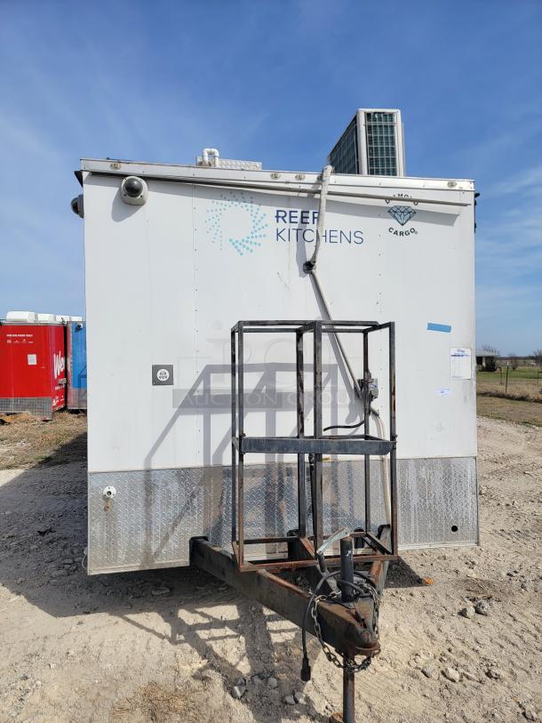 White mobile kitchen unit by Reef Kitchens, marked "UNO Cargo," situated outdoors, with visible wear and hitch for towing.