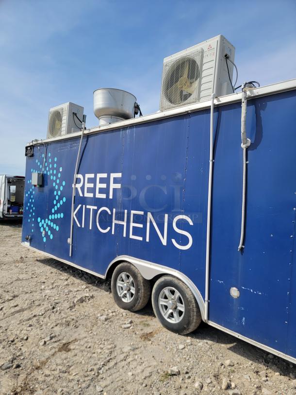Blue mobile kitchen trailer with "REEF KITCHENS" branding. Features rooftop HVAC units. Visible wear on wheels and exterior.