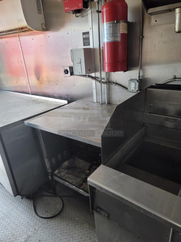 Commercial kitchen setup featuring stainless steel counters, a fire extinguisher, and restaurant equipment in used condition.