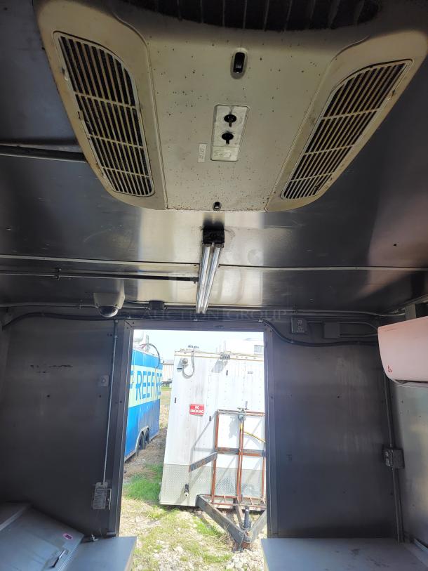 Interior view of a refrigerated trailer with ceiling air vents and fluorescent light. Visible wear on vents, exterior trailers outside.