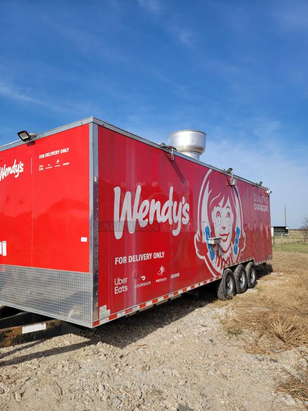 Red Wendy's mobile kitchen trailer with delivery partner logos including Uber Eats and DoorDash, parked on gravel.