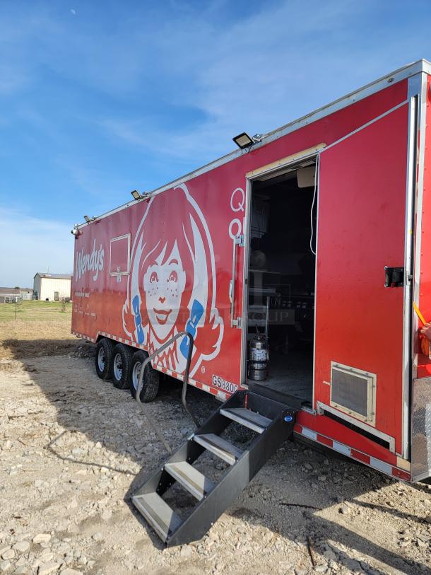 Mobile food trailer with Wendy's branding, red exterior, three axles, fold-out steps, partially open door, good condition.