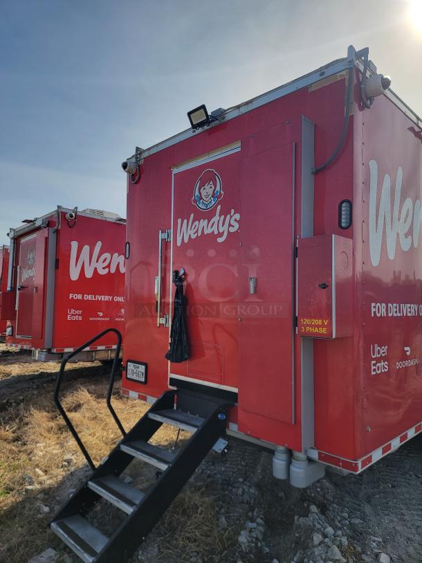 Red mobile kitchen unit with Wendy's branding, delivery service logos, and a utility hook-up. Stairs lead to entrance.