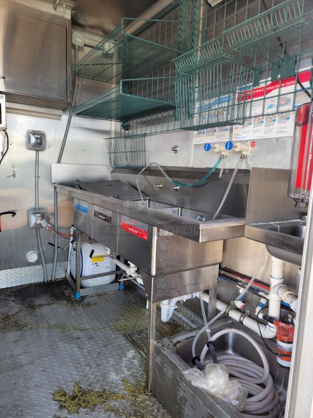 Stainless steel commercial sink setup with multiple basins, faucet controls, and wall-mounted wire shelving above. Good condition.