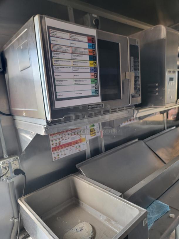 Menumaster commercial microwave, silver, mounted with operation card on door. Well-maintained, industrial kitchen setting.