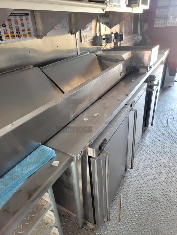 Stainless steel commercial kitchen prep station with dual sink and refrigerated drawers. Slight wear. Ideal for food service.