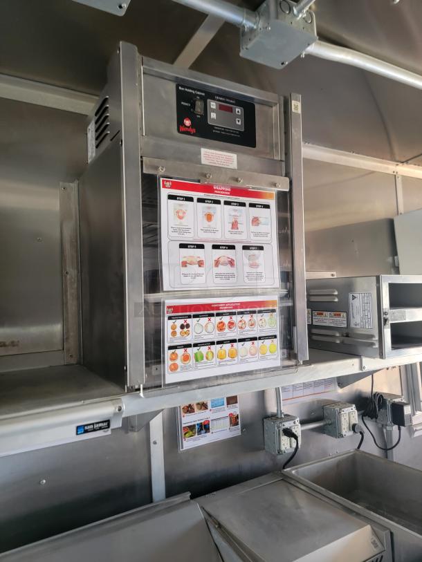 Wendy's bun heating cabinet with control panel and operation instructions mounted in a commercial kitchen setting.