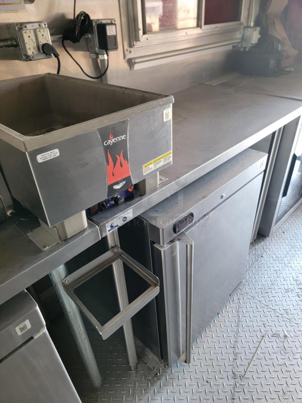 Stainless steel commercial countertop with Wells Cayenne heat lamp, used condition, visible power outlet and mounting brackets.