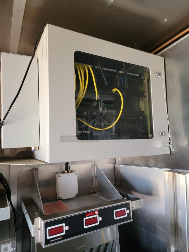 Network server cabinet with visible yellow cables, mounted on wall. Below is a Wendy's appliance with digital displays, metal finish.