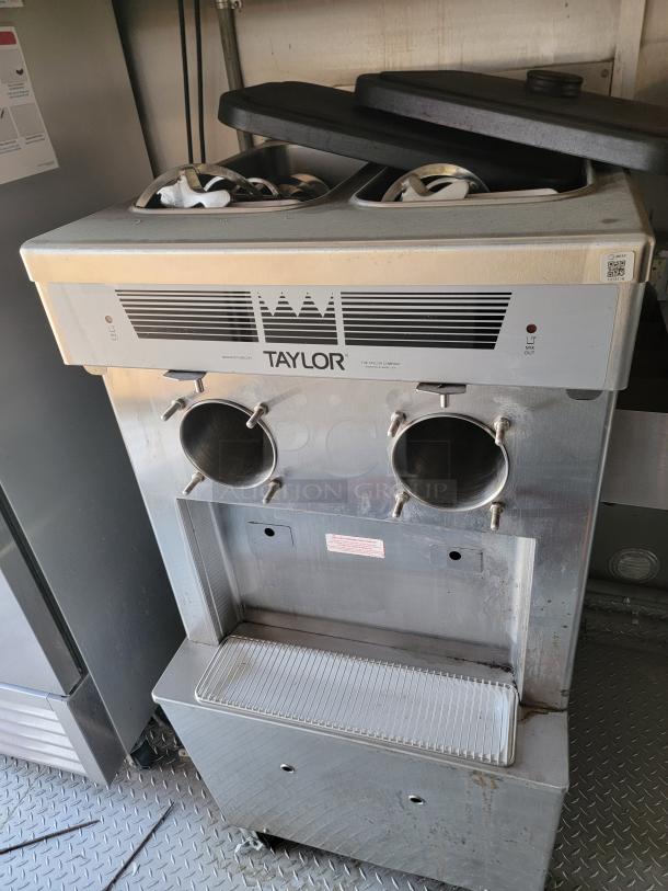 Taylor ice cream machine with dual dispensers, stainless steel body, visible signs of wear, on a mobile base.