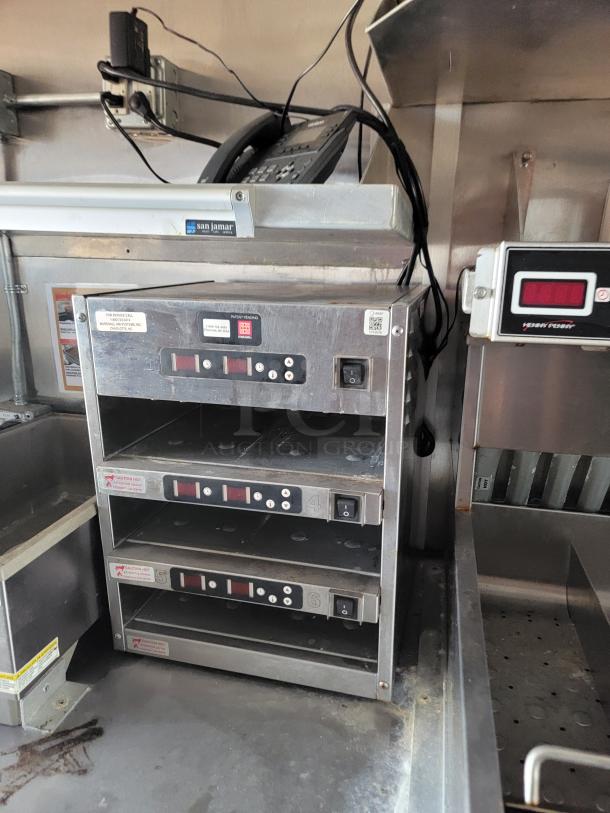Commercial countertop warming drawer with three compartments, labeled controls, some wear visible, stainless steel finish.