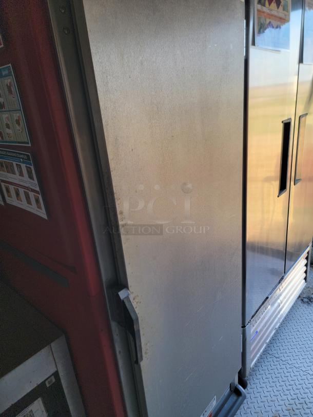Industrial stainless steel refrigerator door with metal handle, showing minor wear and scratches.