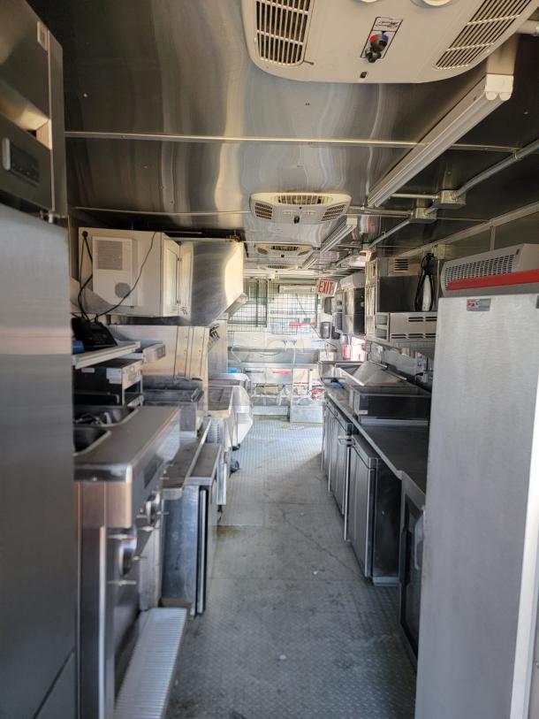Interior view of a commercial food truck kitchen equipped with stainless steel appliances, refrigeration units, and ventilation system. Clean condition.