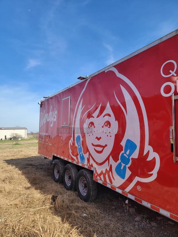 Red Wendy's trailer with logo, parked on grass. Triple-axle wheels, side door visible. Clean exterior.