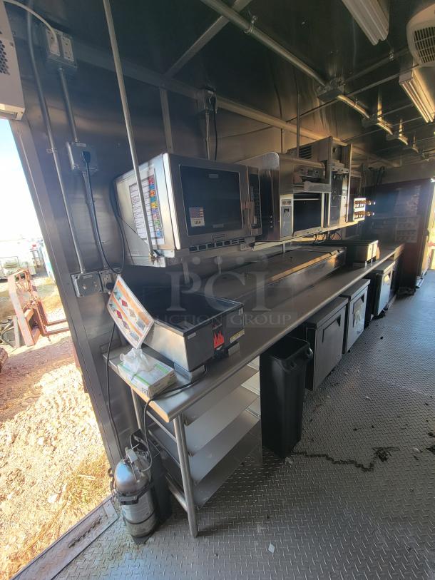 Commercial kitchen setup with stainless steel counters, shelf, microwave, and under-counter appliances. Fire extinguisher, excellent condition.