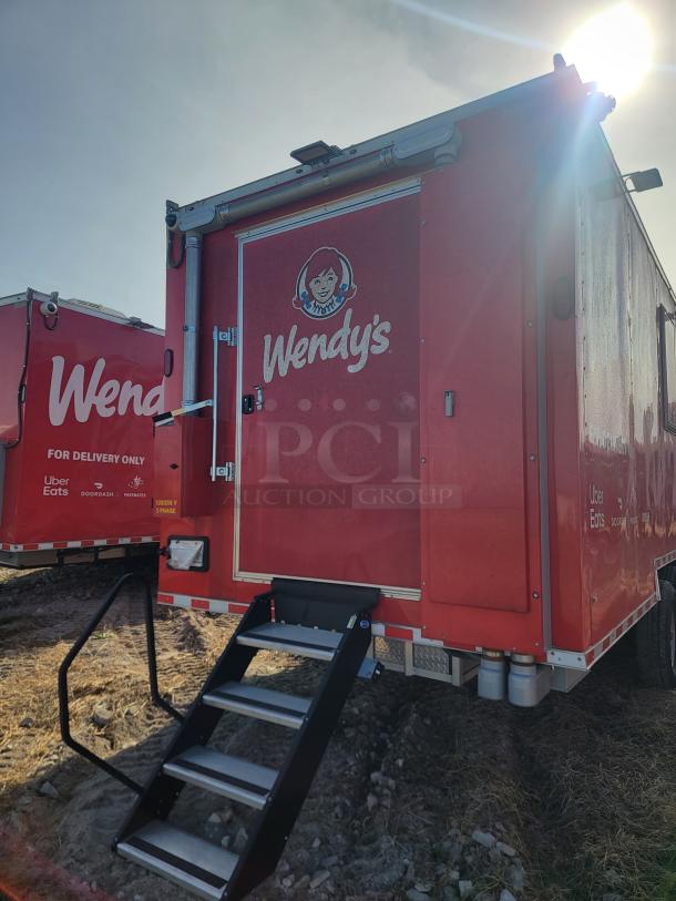 Red Wendy's food delivery truck with logo, foldable stairs, and delivery service decals. Sunlight casts a glare on the right.