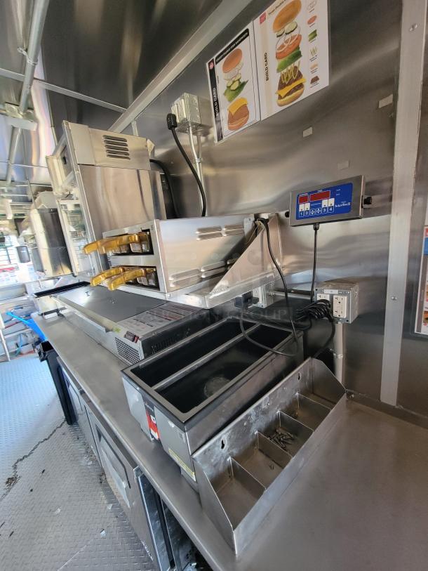 Commercial kitchen equipment with stainless steel countertop, grill, and bun toaster. Includes control panel and storage sections. Clean condition.