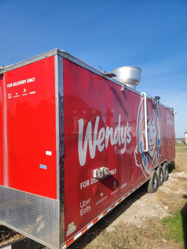 Red Wendy's mobile kitchen trailer branded for delivery with Uber Eats, DoorDash, and Grubhub logos. Visible ventilation system.