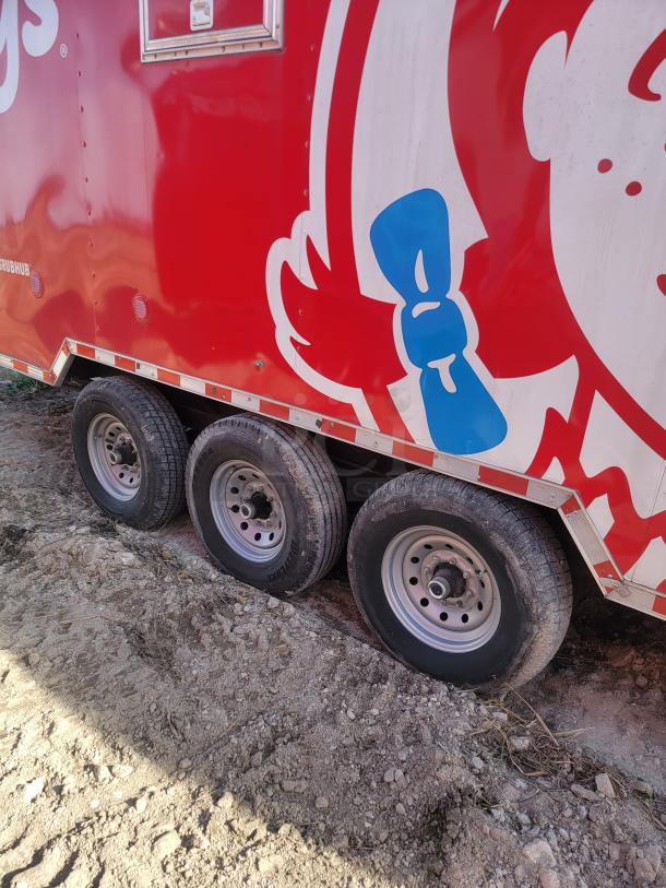Red food trailer with brand logo, triple axle wheels, visible door and hinges, parked on dirt ground. Good condition.