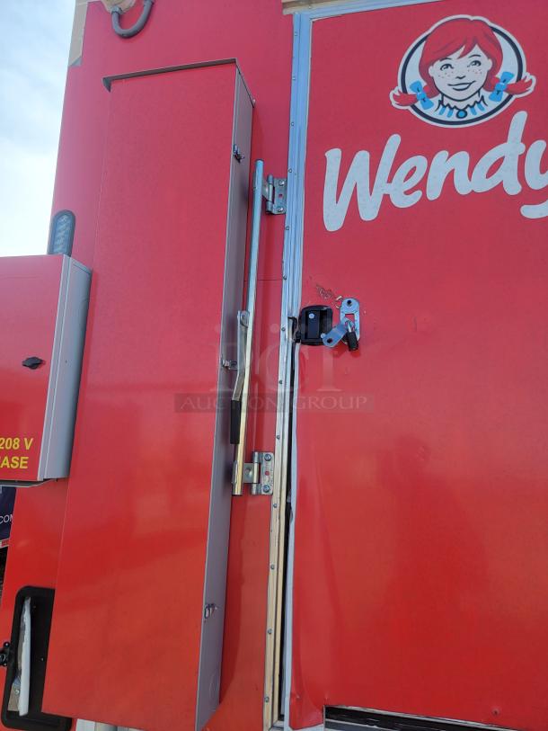 Red Wendy's food truck side panel, featuring logo and door with locks; visible electrical box marked "208 V."