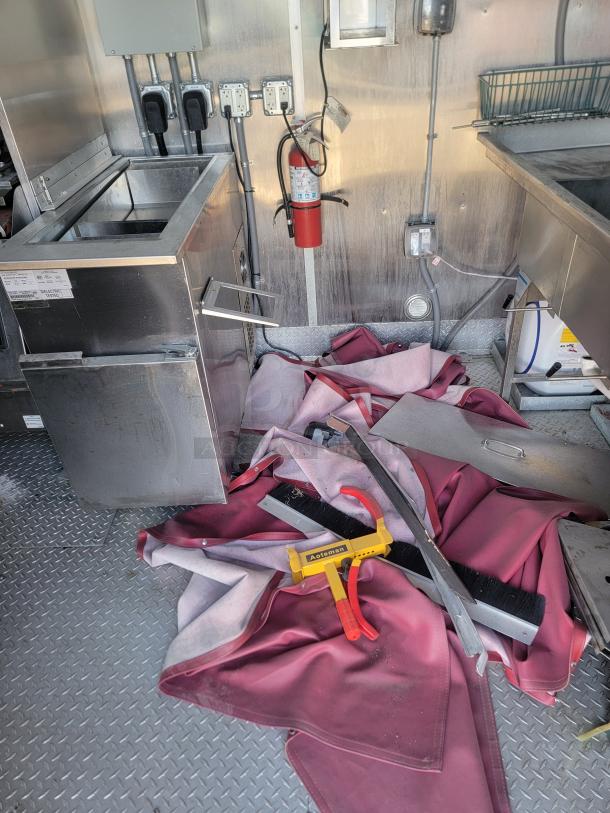 Commercial kitchen equipment with stainless steel cooler, fire extinguisher, and electrical outlets. Includes Aceleman tool and cleaning supplies.