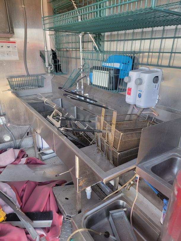 Commercial kitchen sink with multiple compartments, steel countertop, wire baskets, and a water heater. Good condition.