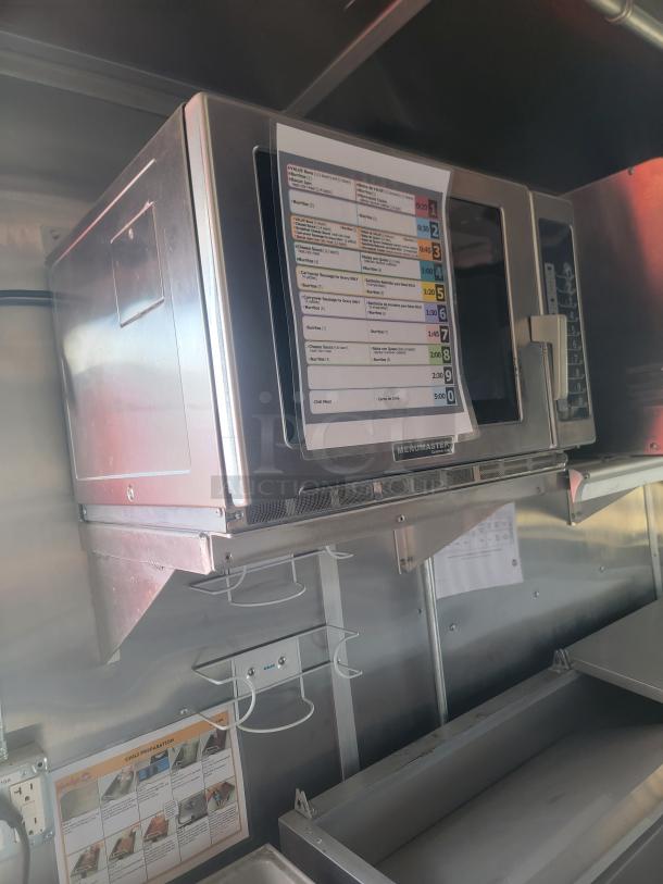 Stainless steel microwave oven with menu guide attached, mounted on a kitchen wall. Features digital controls and chrome finish.