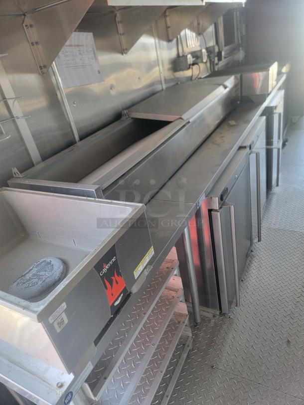 Commercial kitchen setup with stainless steel counters, a Cayenne appliance, and storage shelves. Appears in good condition.