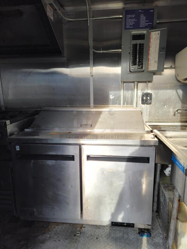 Commercial stainless steel two-door refrigerator with a prep surface; features visible wear, ideal for food service setups.