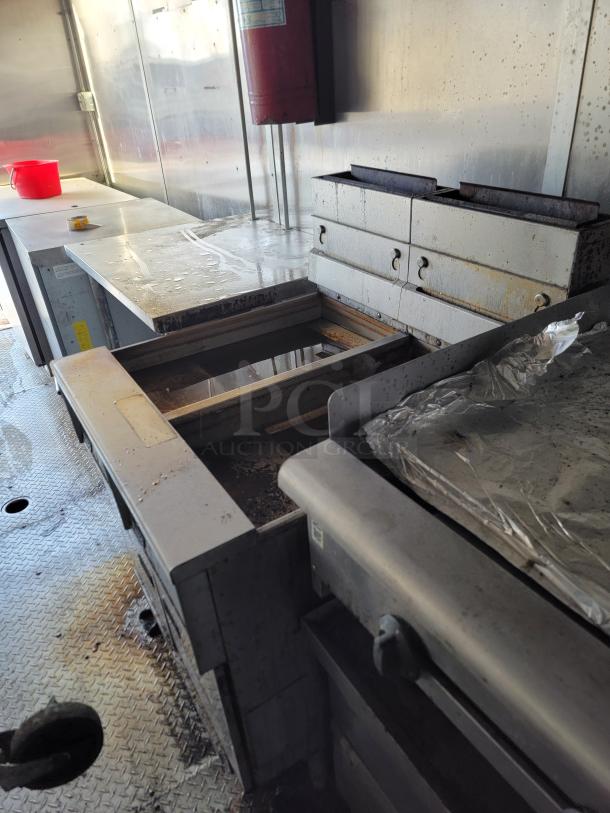 Industrial kitchen setup with stainless steel counters, deep fryer, and storage compartments. Visible wear and corrosion.