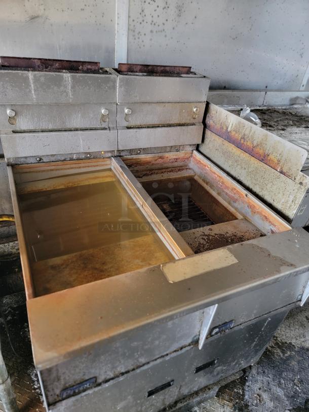 Industrial fryer, stainless steel, with dual oil vats, visible wear and rust, suitable for commercial kitchen use.