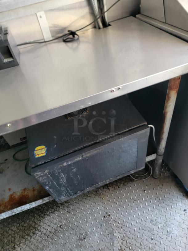 Commercial-grade countertop with under-counter storage unit. Metal surface, visible wear. "Where’s My Burger" sticker.