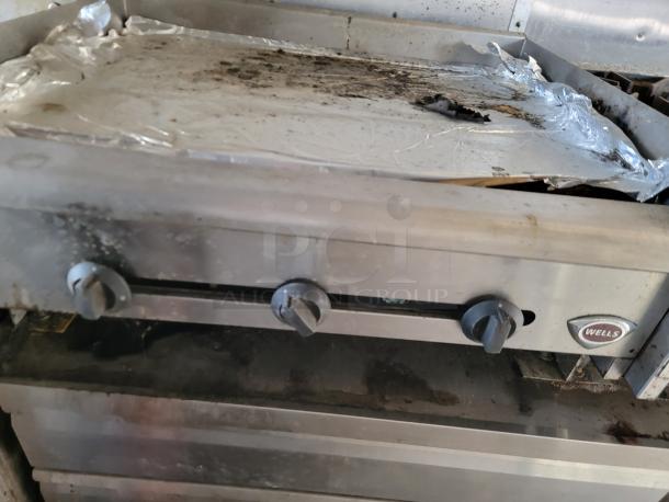 Wells griddle with three control knobs, stainless steel casing, and foil-covered top surface. Shows signs of heavy use.
