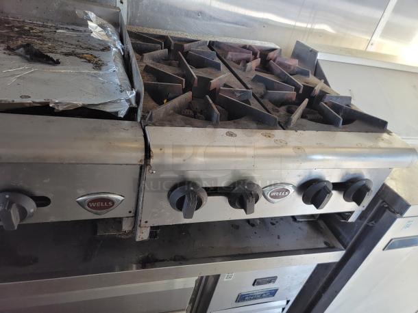 Wells commercial stove with four burners, visible wear and tarnish, featuring control knobs and Wells branding.