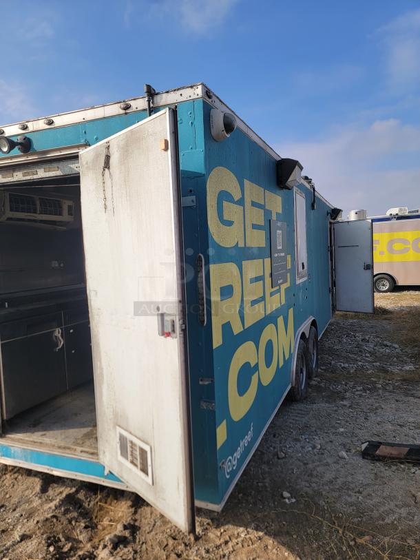 Blue mobile trailer with "GET REEL" in large yellow text. Side door open, revealing interior kitchen setup. Slight exterior wear.