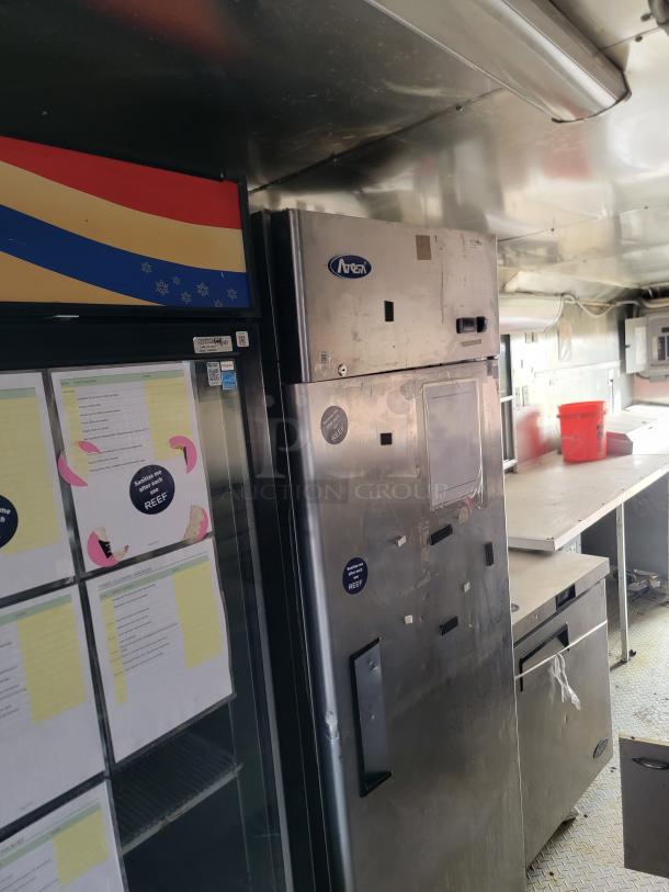 Stainless steel commercial refrigerator with Arneg branding, visible wear and stickers. Features utility shelves inside.