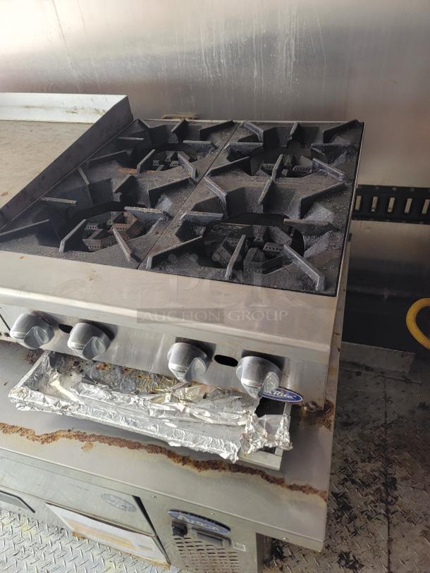 Commercial four-burner gas range with control knobs. Shows signs of use; some rust and residue visible. Ideal for professional kitchens.