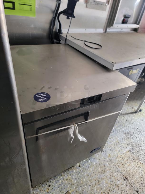 Stainless steel commercial refrigerator; features a "Sanitize me after each use" sticker. Used condition, some surface wear.