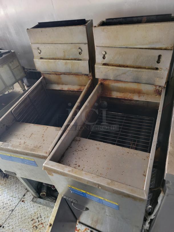 Industrial deep fryer with twin units, stainless steel, worn condition, visible rust and grease, safety warnings on front.