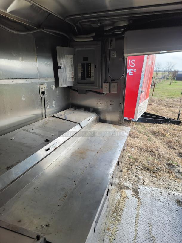 Interior of metal mobile kitchen with stainless steel countertop and electrical panel. Visible dirt and signs of wear.