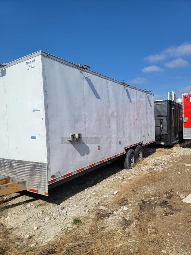 White Titanium cargo trailer with dual axles, side vents, visible wear, and wear on the exterior. Marked "Titanium Cargo Trailers LLC."