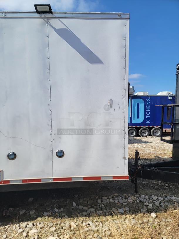 White utility trailer with visible dents and a mounted light. Reflective strip on the bottom edge. In used condition.
