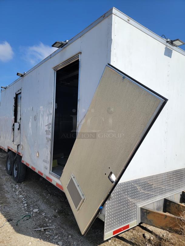 Damaged white cargo trailer with a detached side door, showing wear. Dual axle, exterior floodlights, diamond-patterned lower panel.
