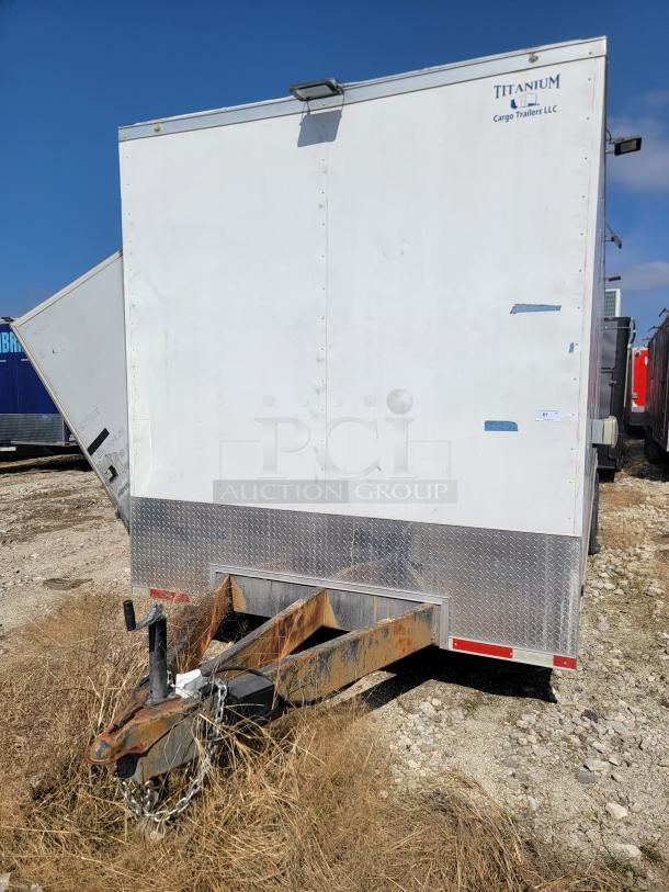 Titanium Cargo Trailers LLC trailer, white exterior with diamond plate accents. Rusted hitch, visible signs of wear.