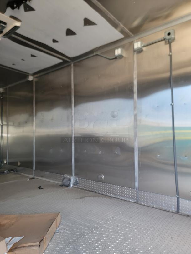 Interior of a metallic trailer, showing diamond plate flooring and unfinished walls with electrical wiring visible.