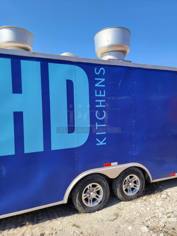 Blue HD Kitchens mobile trailer with dual vents, resting on a gravel surface. Features tandem wheels and bold lettering.
