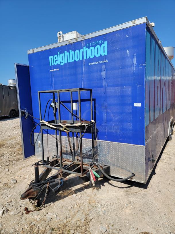 Blue mobile kitchen trailer with "neighborhood kitchens" branding, visible utility connections, and metal towing frame.